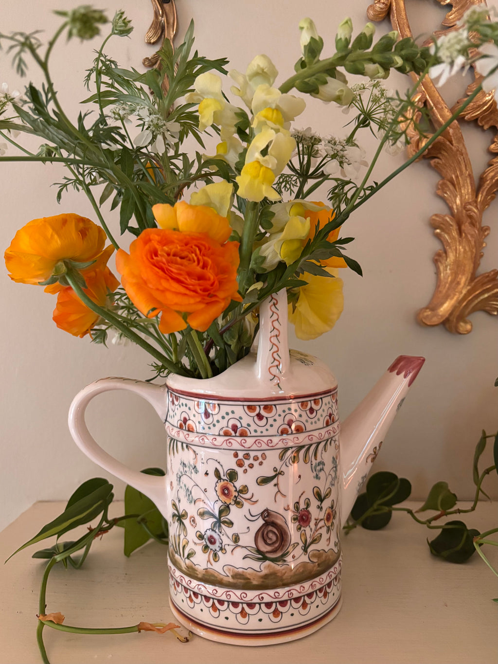 Side view of hand-painted ceramic watering can showing domed lid, snail motif, and folk art floral border bands.