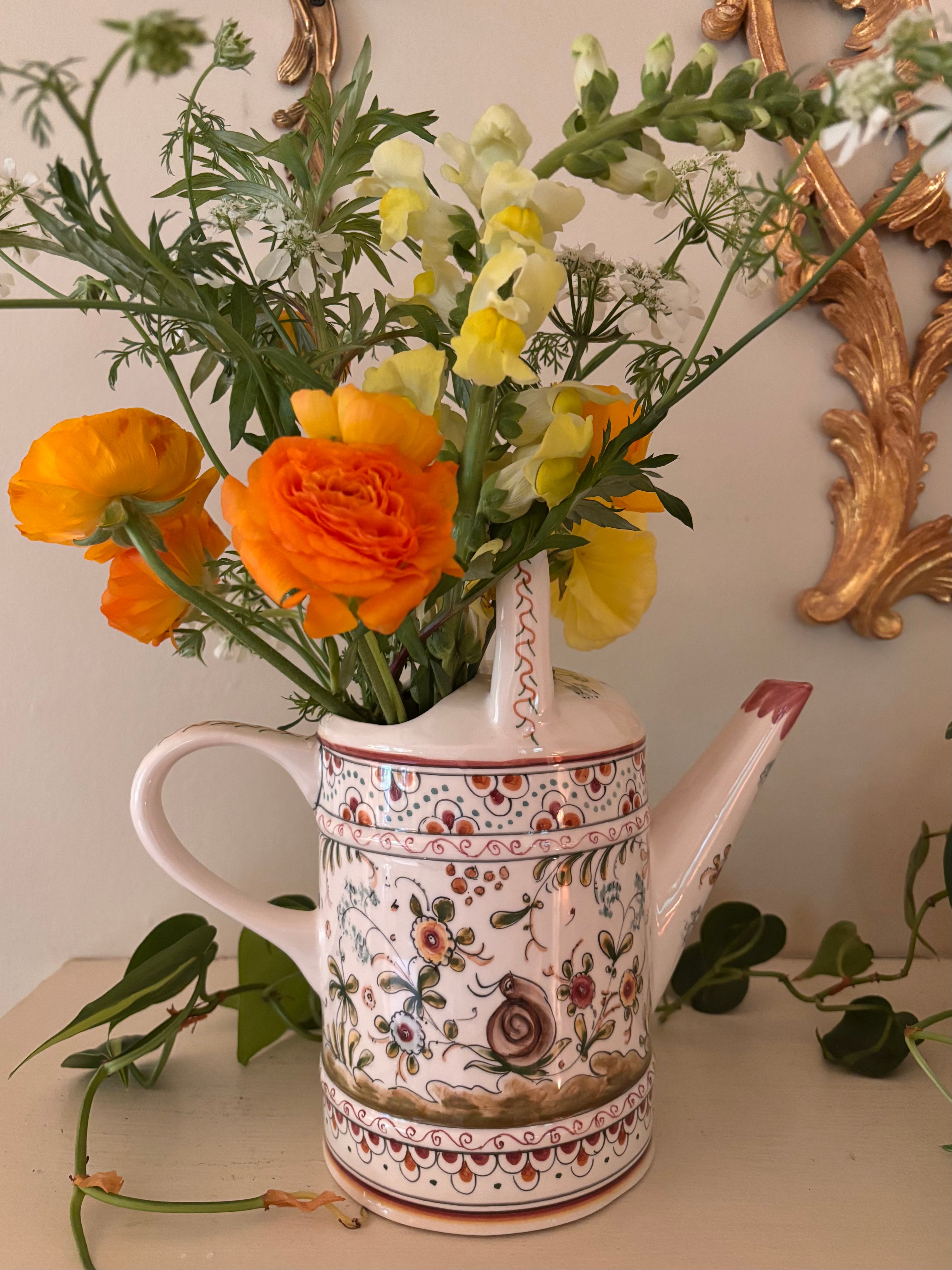 Side view of hand-painted ceramic watering can showing domed lid, snail motif, and folk art floral border bands.