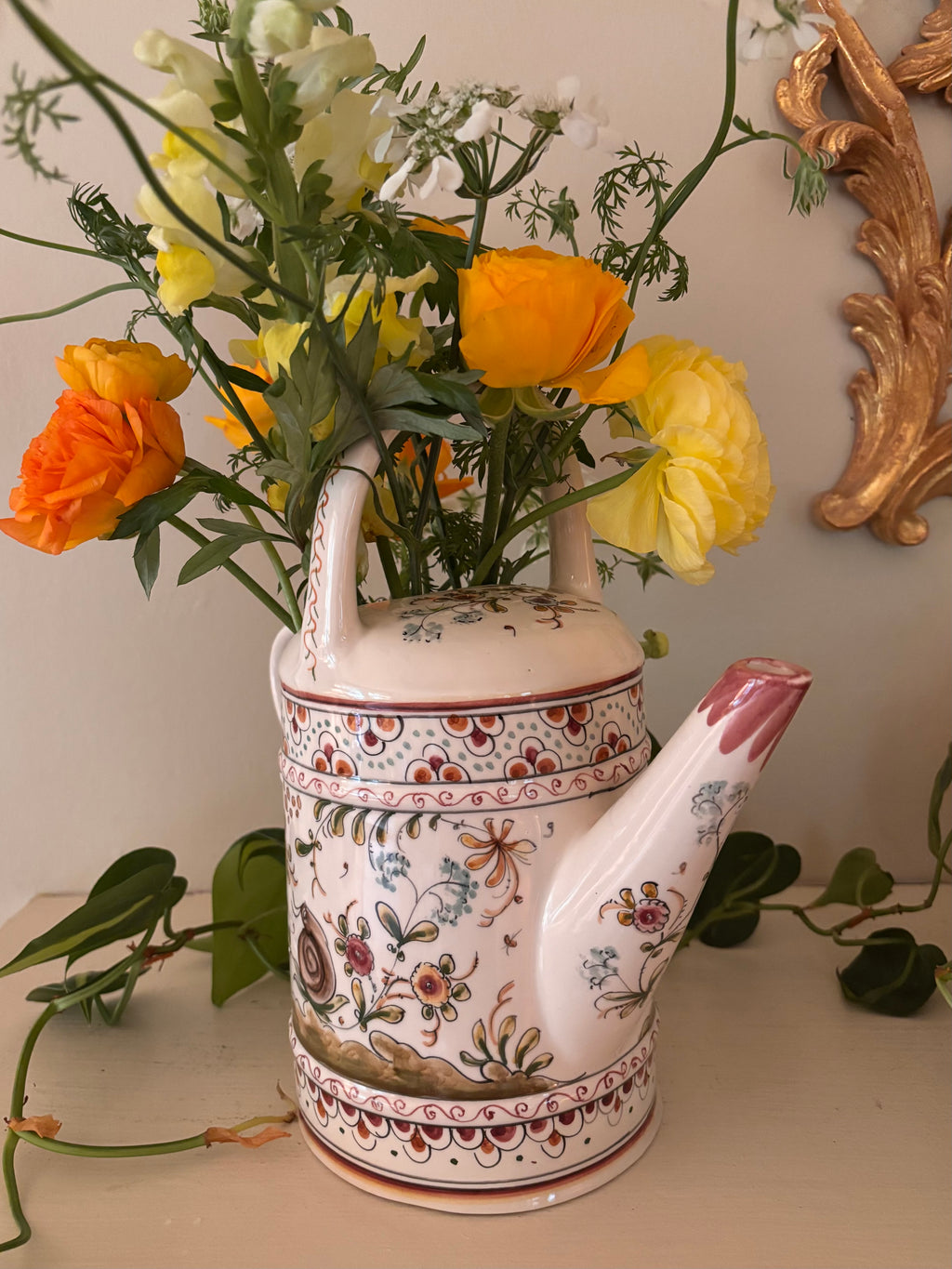 Front view of hand-painted ceramic watering can with bird motif on lower body and terracotta scallop border.