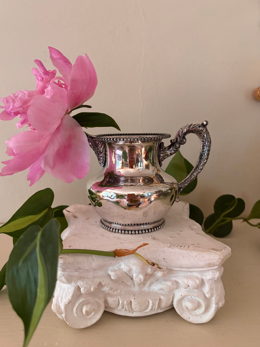 Small polished silver-plate cream pitcher with beaded rim and base, ornate scroll handle with ball finial.