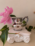 Small polished silver-plate cream pitcher with beaded rim and base, ornate scroll handle with ball finial.