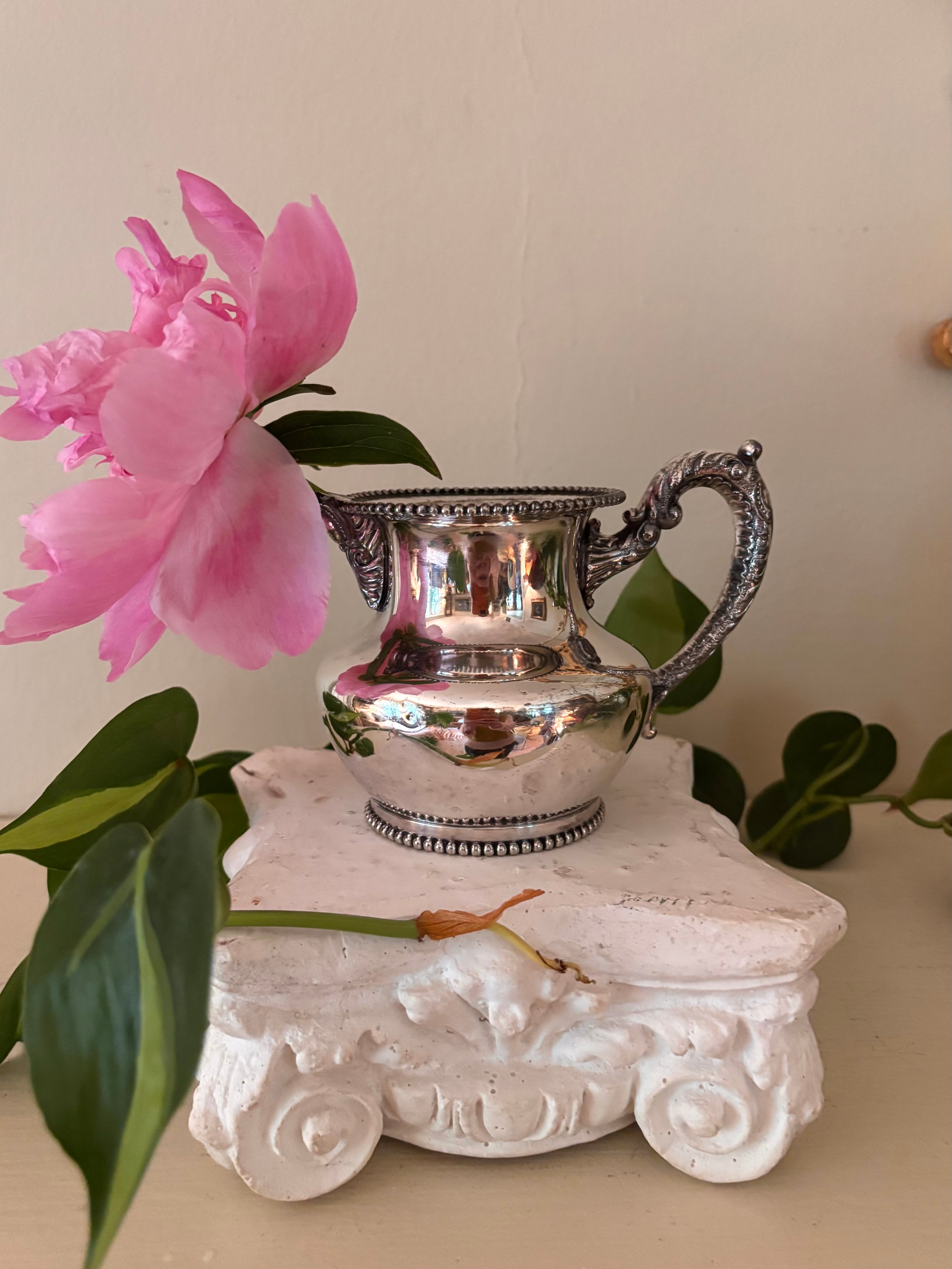 Small polished silver-plate cream pitcher with beaded rim and base, ornate scroll handle with ball finial.