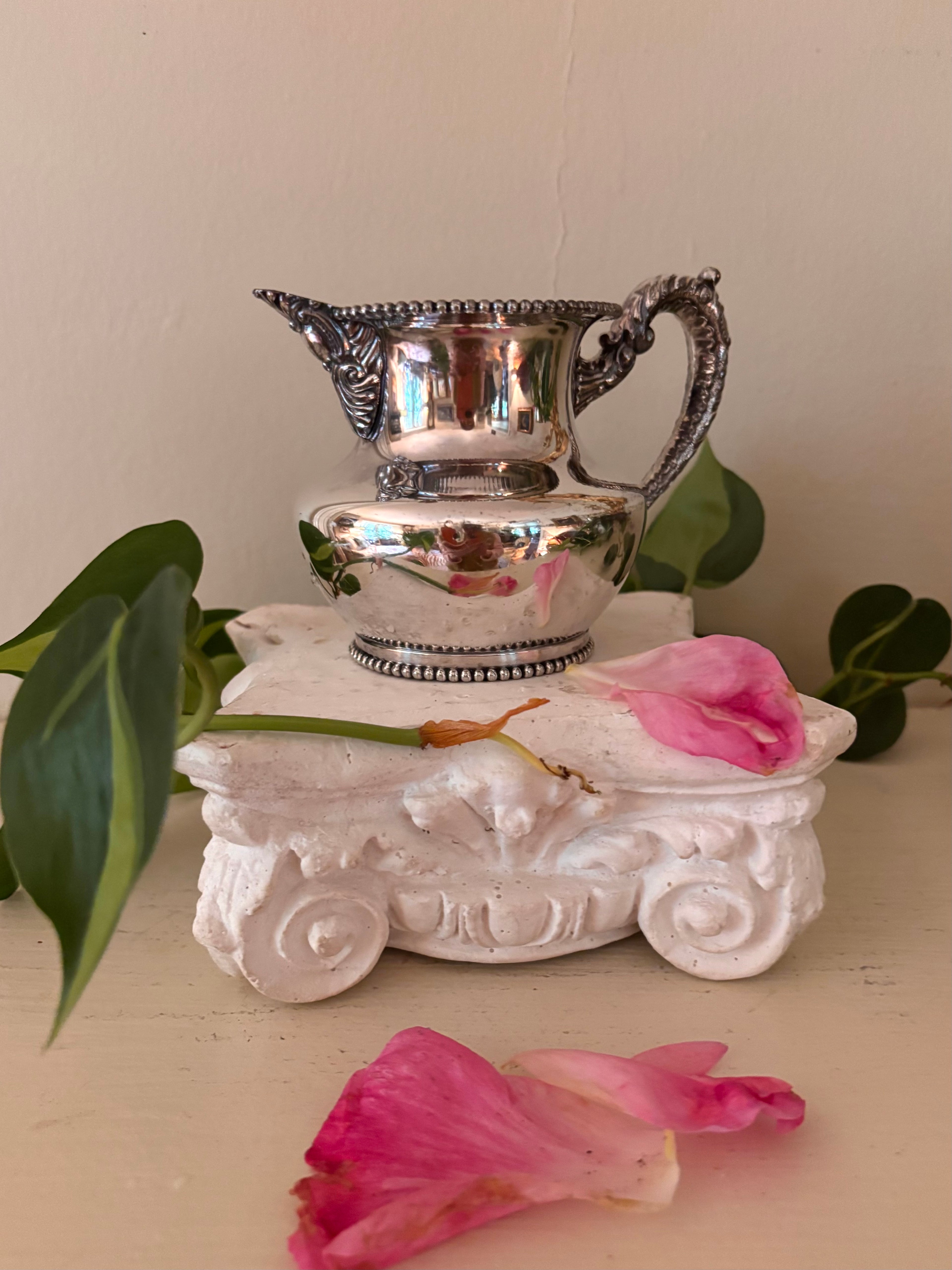 Three-quarter view of silver-plate cream pitcher with sculpted acanthus handle and scroll details, beaded rim and base.