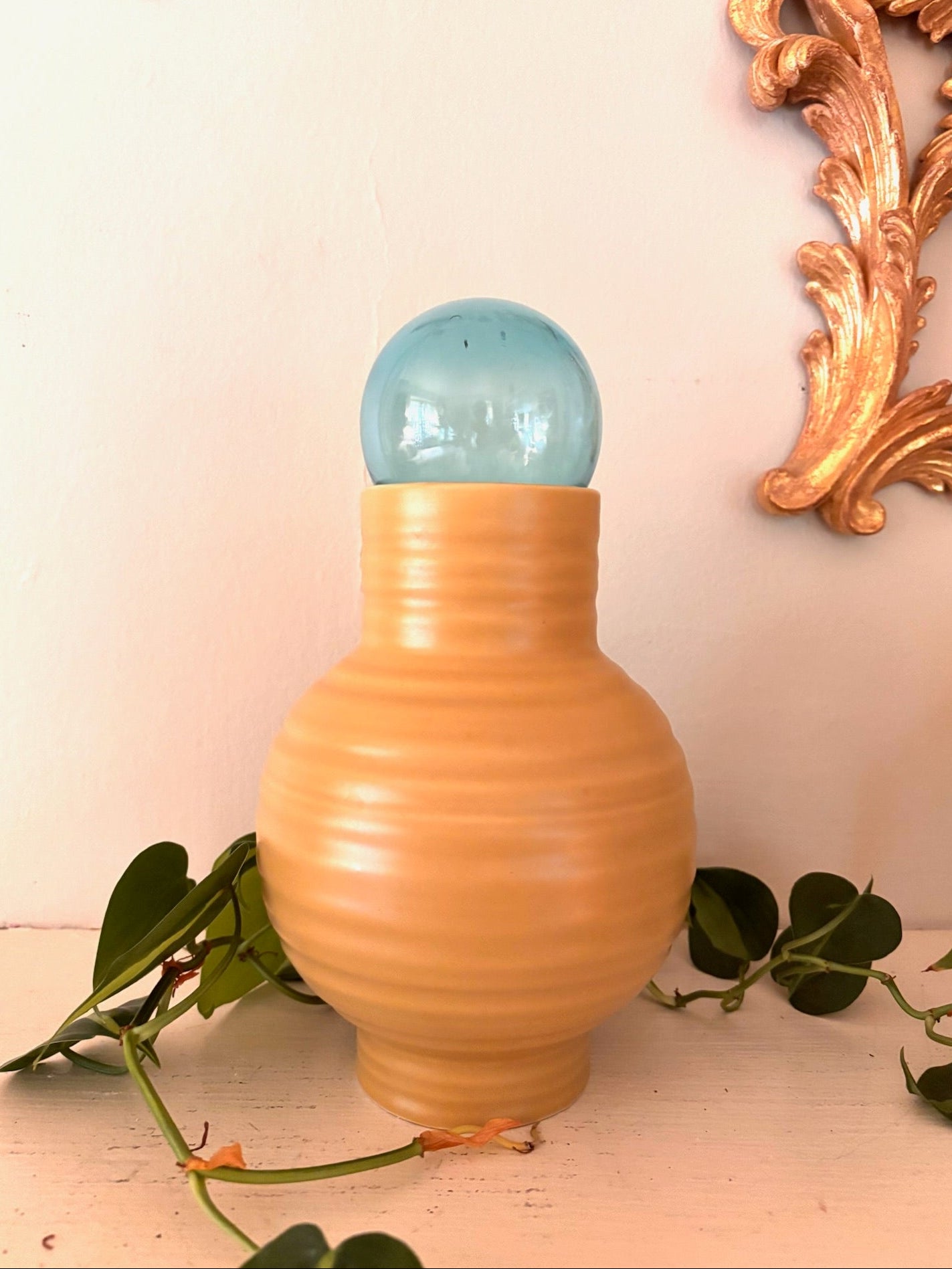 Round ribbed peach matte ceramic vase with pale teal glass orb resting in narrow neck opening.
