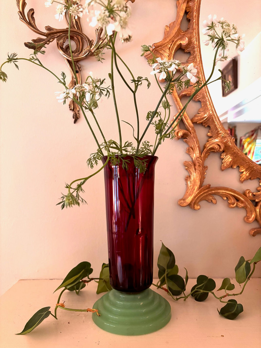 Tall ruby red ribbed glass vase seated on a stepped jade green ceramic pedestal base.