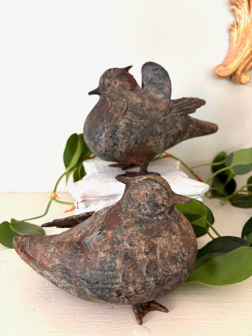Two cast metal bird figurines with rust and verdigris patina, one with folded wings and one with raised wings.