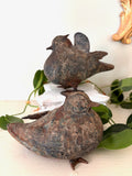 Two cast metal bird figurines with rust and verdigris patina, one with folded wings and one with raised wings.
