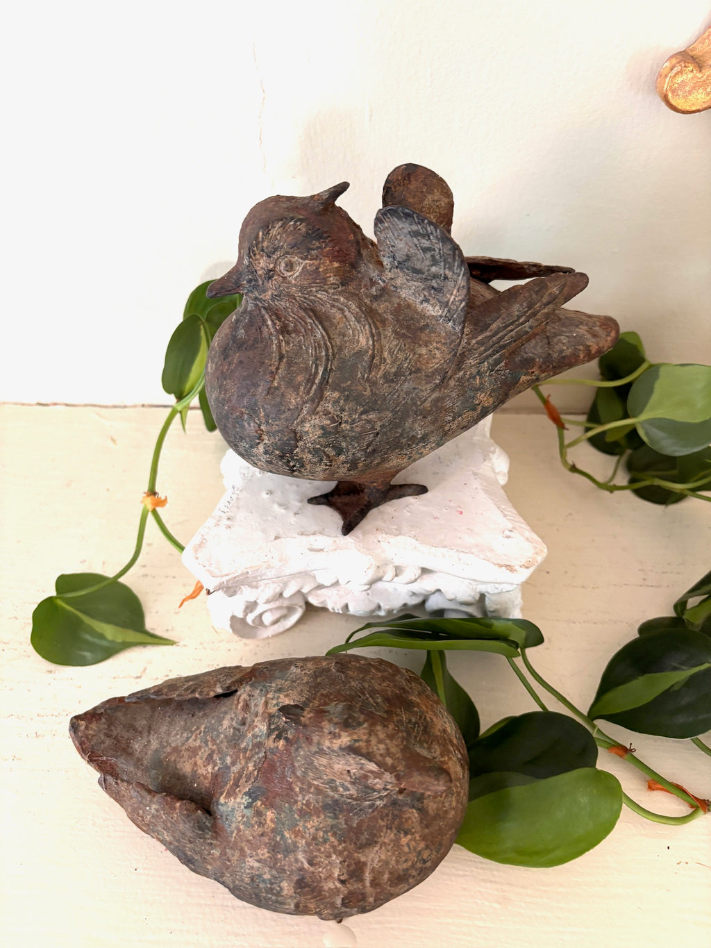 Two patinated cast metal birds, one upright with folded wings and one resting on its side.