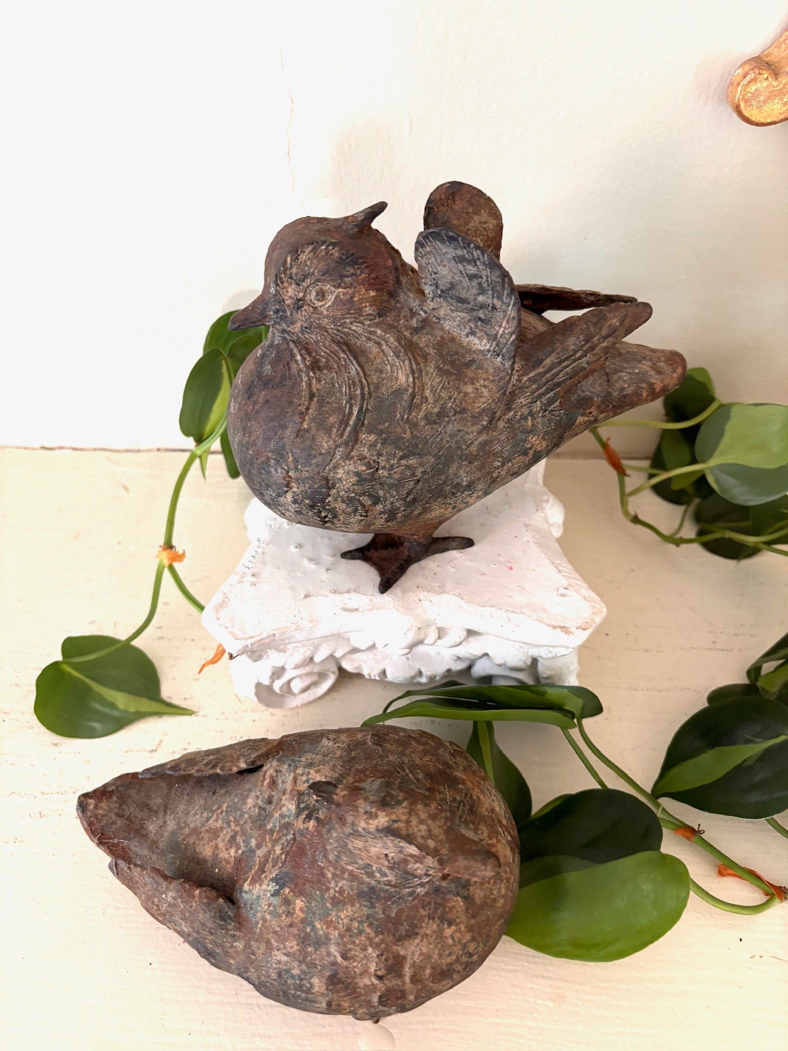 Two patinated cast metal birds, one upright with folded wings and one resting on its side.