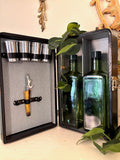 Open travel bar case showing chrome cups, amber-handled corkscrew, and two square green glass bottles.