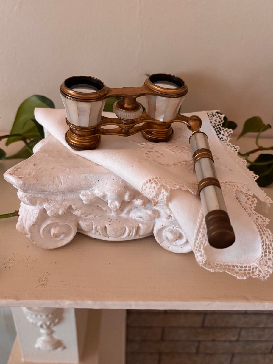Antique opera glasses with iridescent mother of pearl bodies and brass hardware, with an extending mother of pearl and brass handle, resting on a white plaster architectural fragment with a linen handkerchief