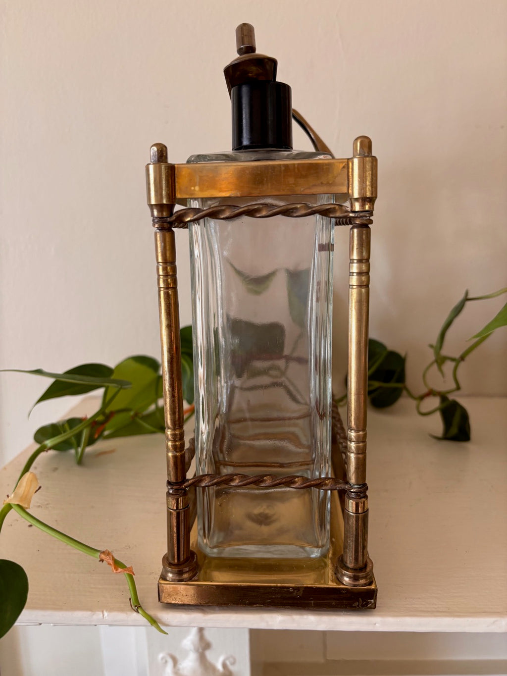 Side view - Antique brass tantalus liquor caddy with three glass decanters stenciled in gold with spirit names including Gin and Scotch, with twisted rope rail detailing, turned corner columns, and Bakelite stoppers