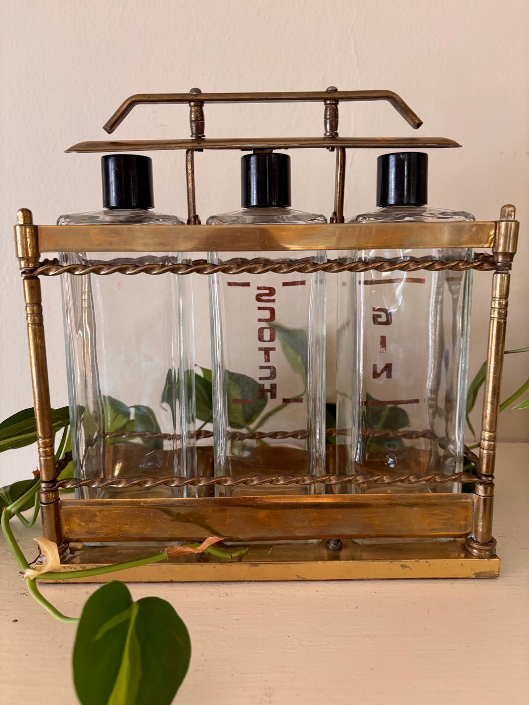 Rear view - Antique brass tantalus liquor caddy with three glass decanters stenciled in gold with spirit names including Gin and Scotch, with twisted rope rail detailing, turned corner columns, and Bakelite stoppers