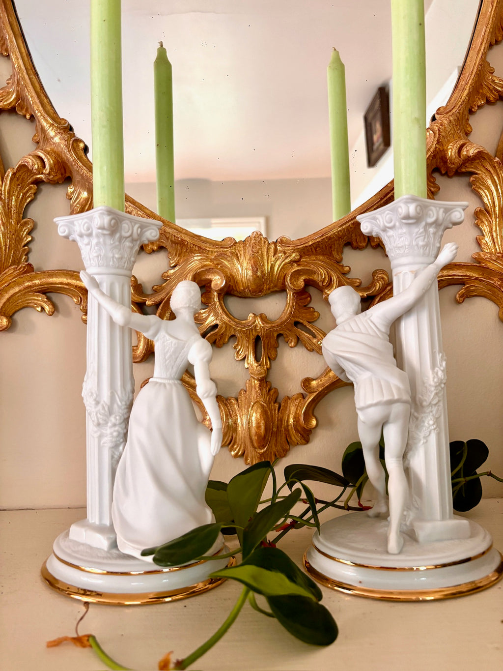 Back view of a bisque porcelain candle holder with a fluted column and a figure in period dress at the base.