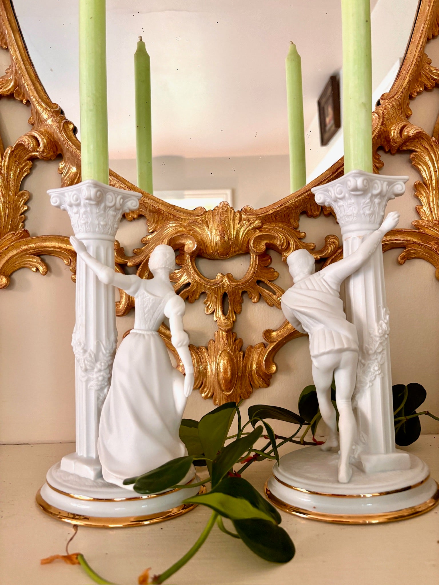 Back view of a bisque porcelain candle holder with a fluted column and a figure in period dress at the base.