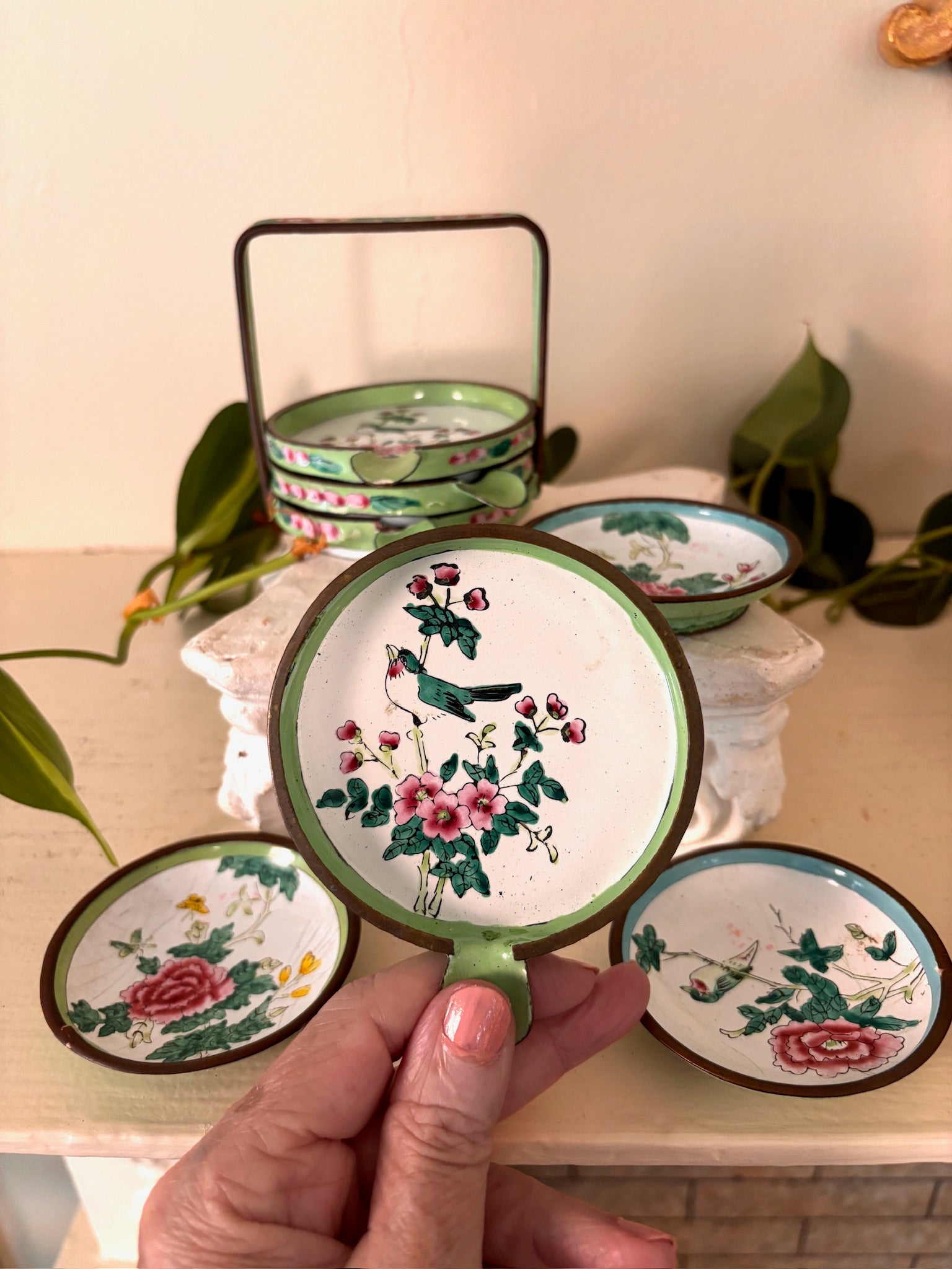 Green enamel basket holding stacked enamel dishes with a peony and bird dish in front.
