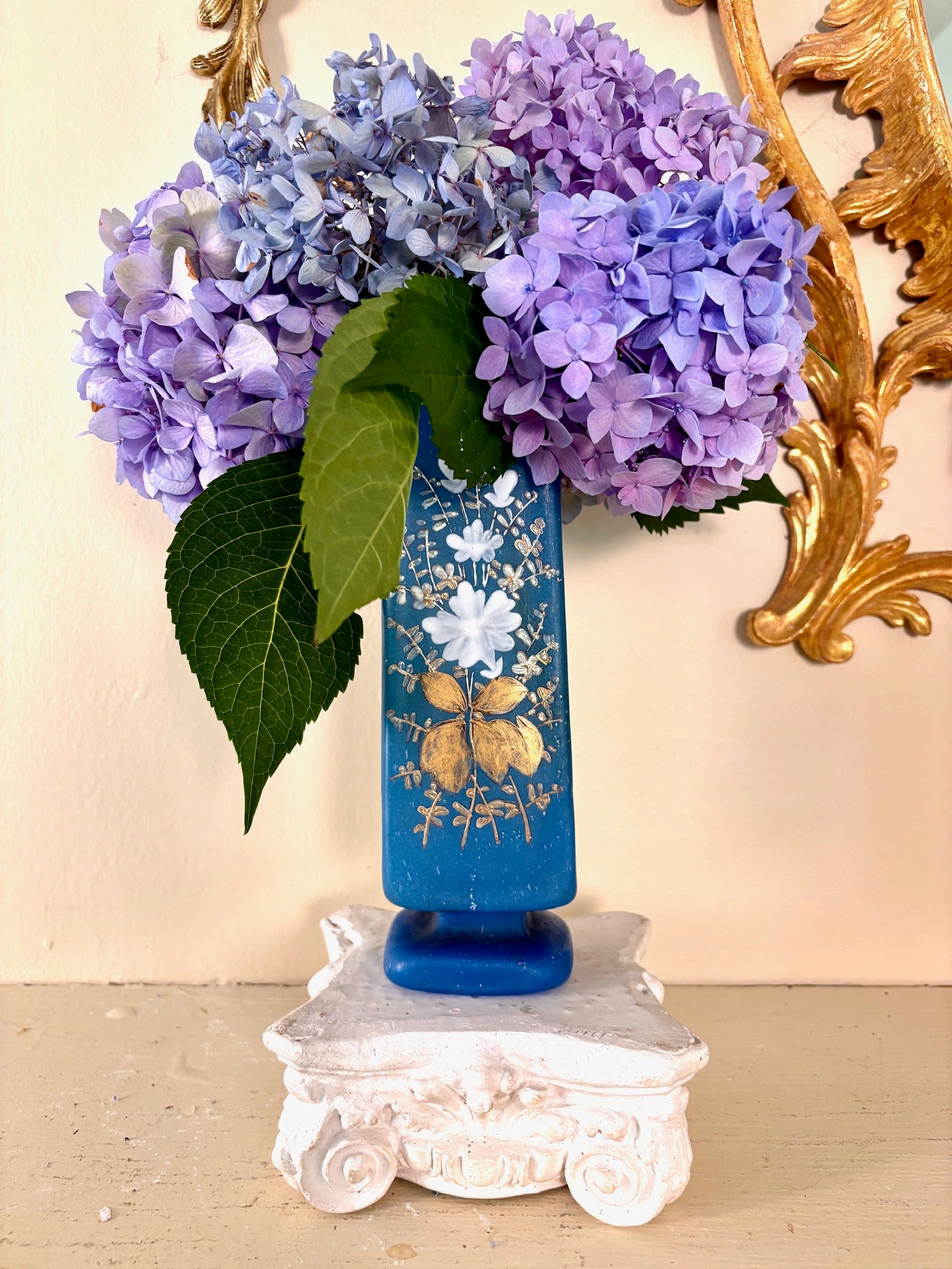 Tall frosted blue glass vase with hand-painted white florals and gold gilt foliage, on a footed base.
