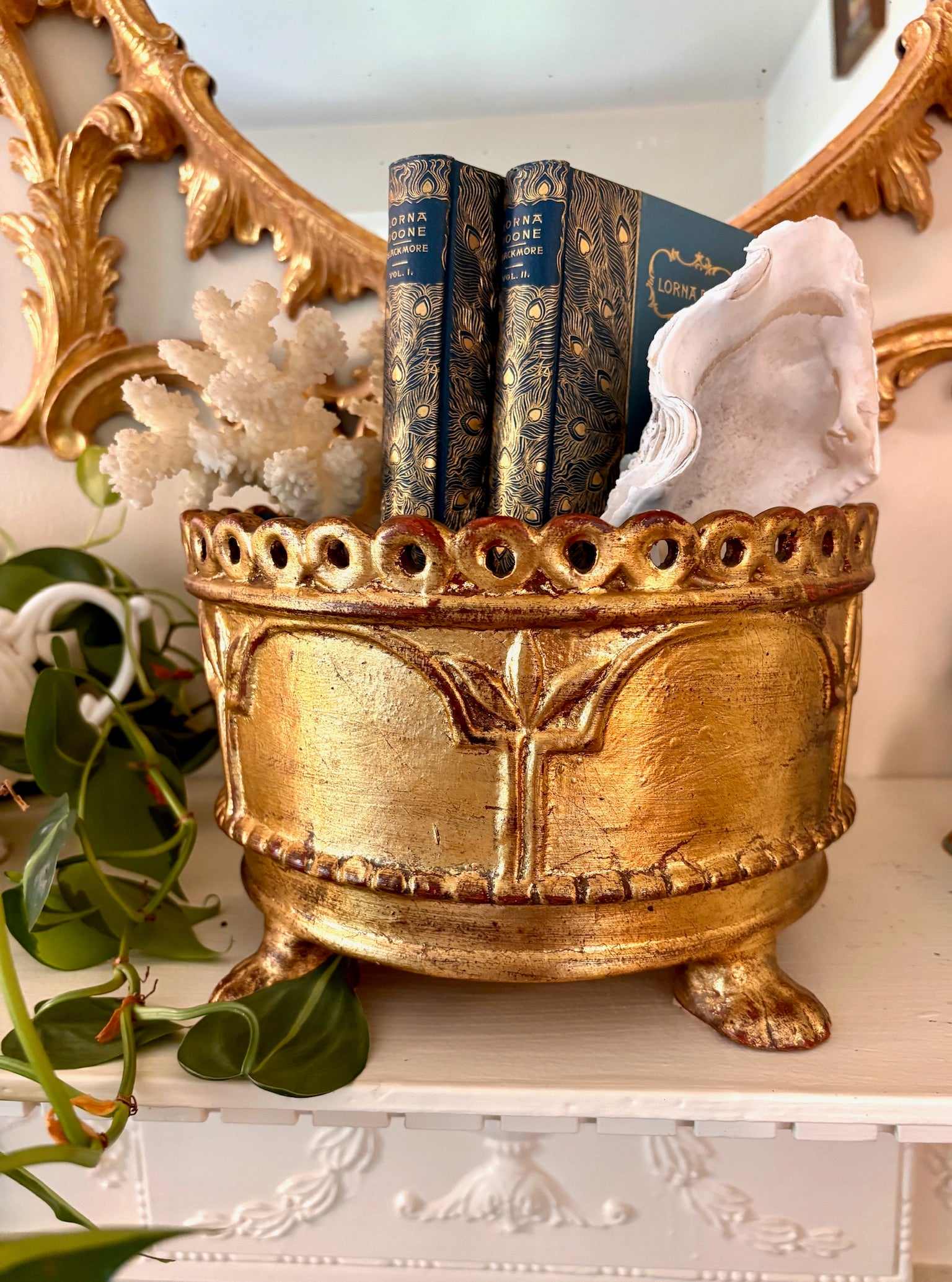Gilded ceramic cachepot with pierced rim, turquoise interior, and scroll feet, holding books and a shell.