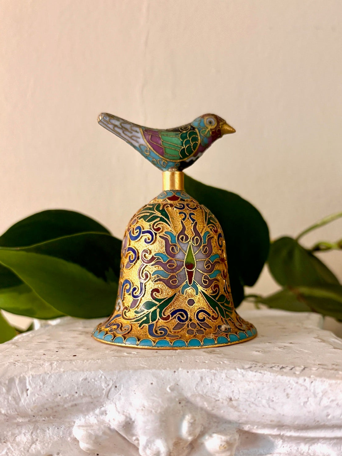 Gilt cloisonné enamel bell with colorful scrollwork and a bird finial on top.