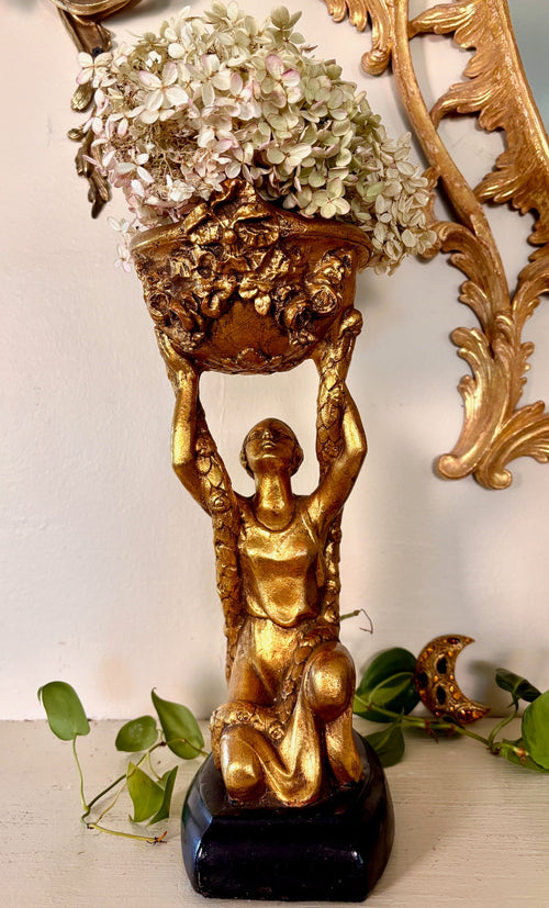 Gilded figural planter stand, a kneeling robed figure holding a floral-relief bowl overhead.