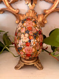 Hand-painted egg with dense coral and pink florals on a dark ground, on a small gilt metal footed base.