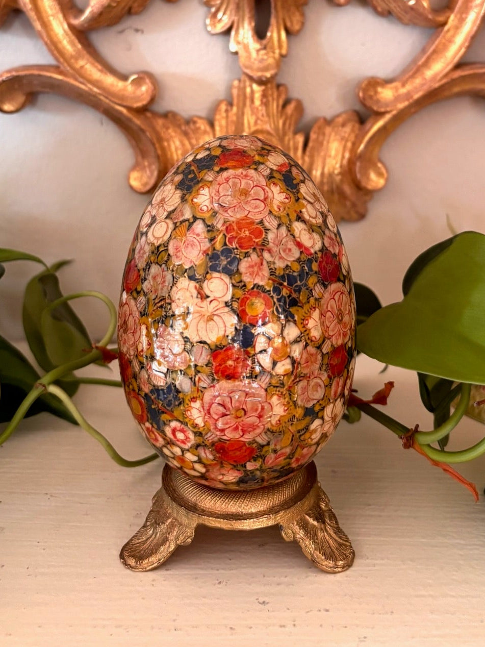 Hand-painted egg with dense coral and pink florals on a dark ground, on a small gilt metal footed base.