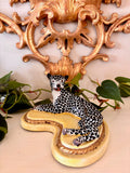 Reclining ceramic leopard hand-painted with black spots on white, on a yellow base with a gilt rope edge.