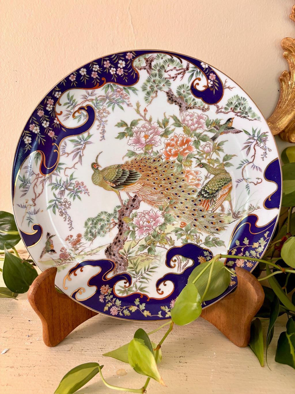 Japanese porcelain plate with cobalt blue border and hand-painted peacocks among peonies and pine branches.