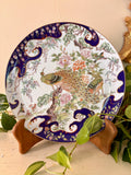Japanese porcelain plate with cobalt blue border and hand-painted peacocks among peonies and pine branches.