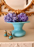 Turquoise opaline glass compote with a wide flared bowl on a pedestal foot, filled with purple hydrangeas.