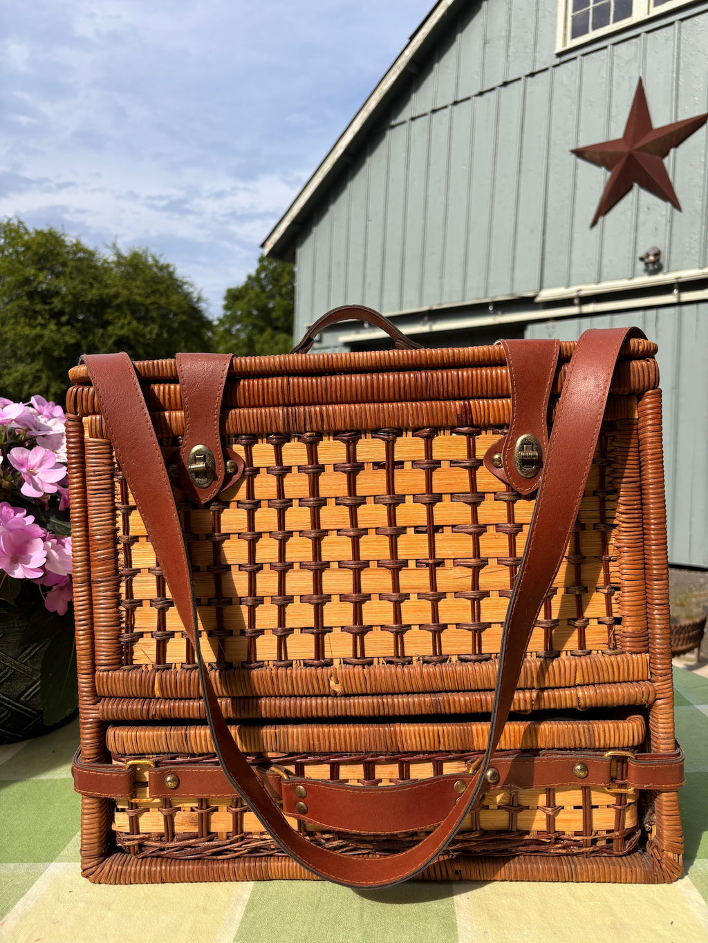 Closed wicker picnic basket with brown leather straps, brass latches, and a carrying strap.