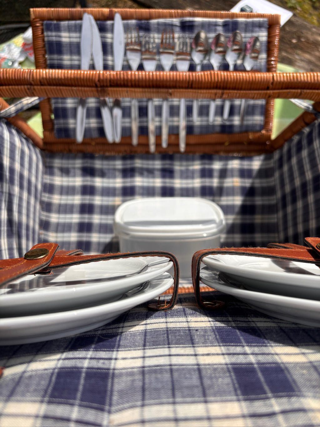 Close-up of stainless flatware held in a leather strap band inside a wicker picnic basket.