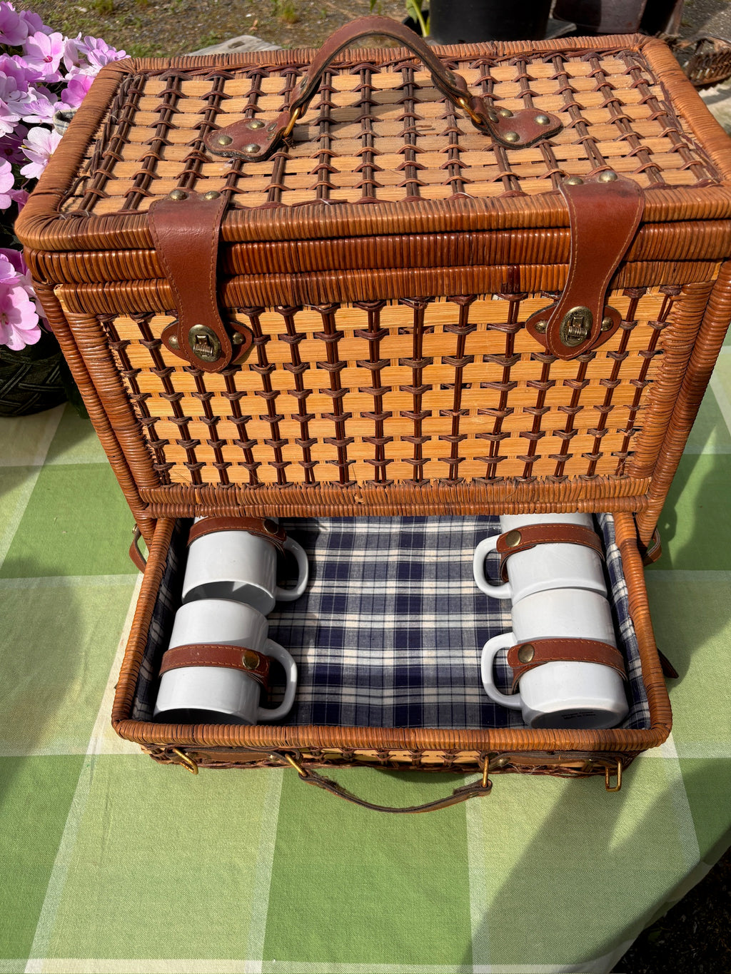 Wicker picnic basket drawer with four white ceramic mugs secured by leather straps.