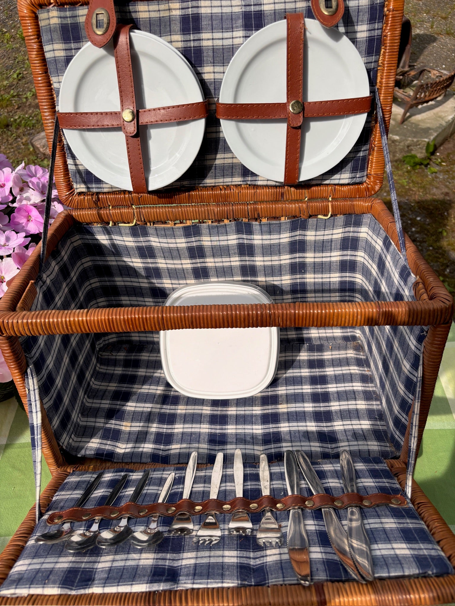 Wicker picnic basket open to show four ceramic plates, flatware, and a storage container inside.