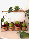 Caddy of eight small woven rattan baskets in a black metal grid frame with a bamboo handle bar across the top.